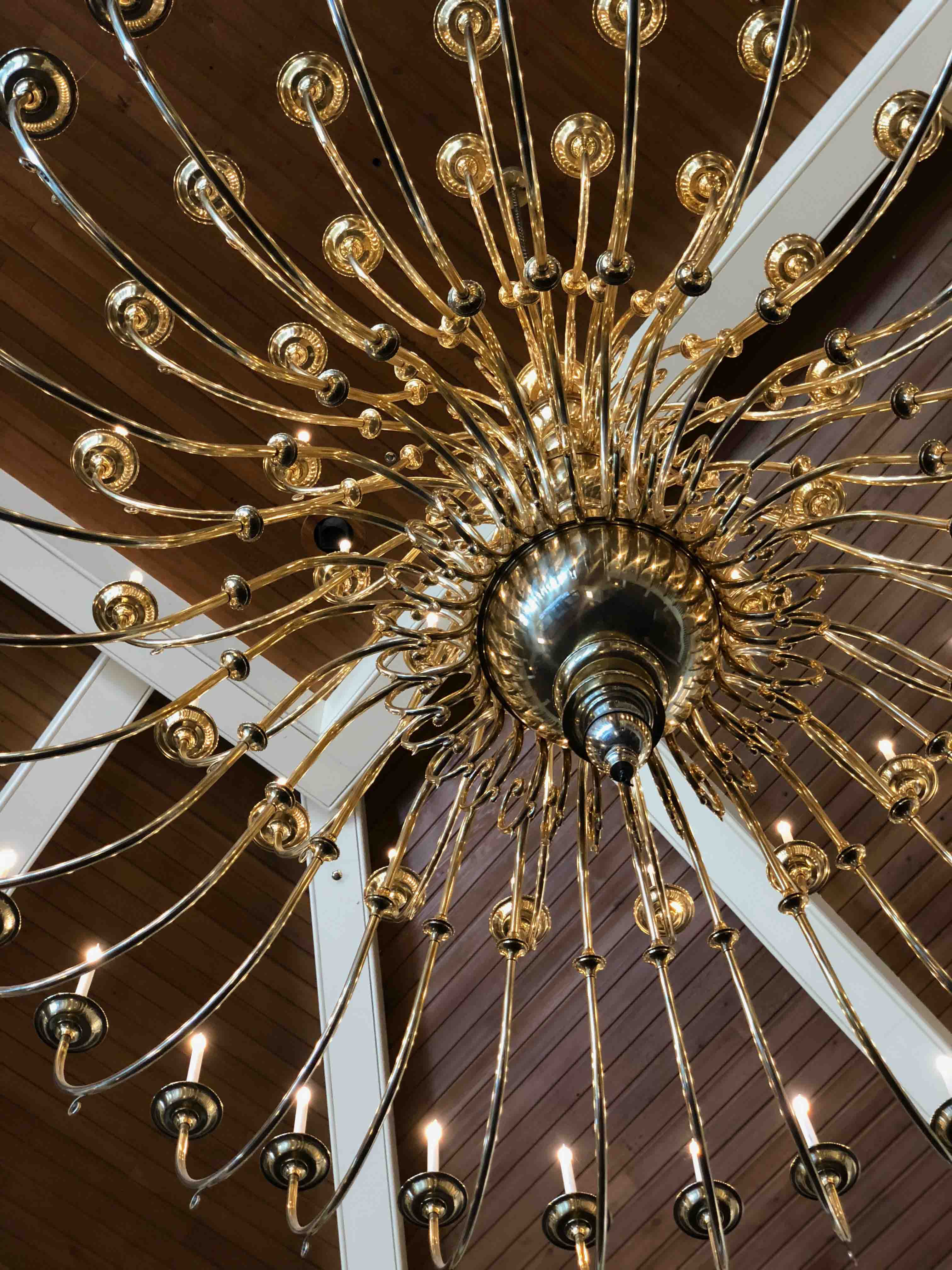 Looking up at a bronze chandellier against a wood ceiling